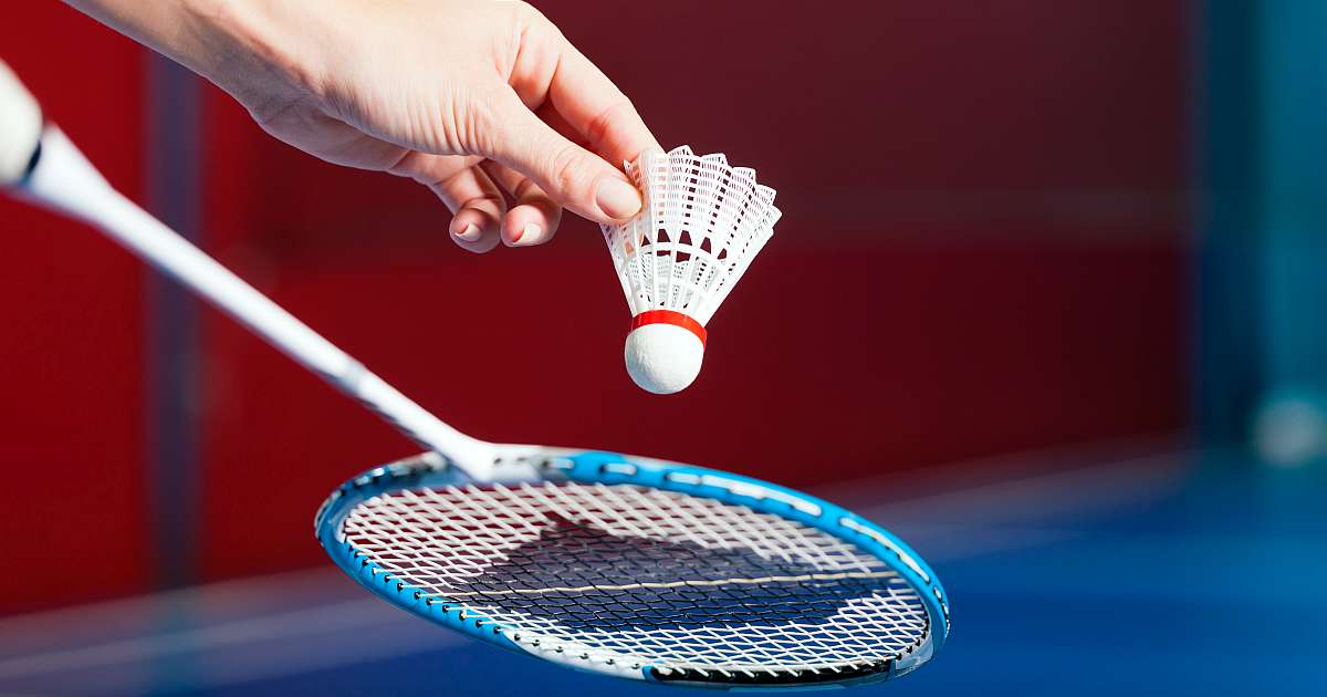 Eine Hand hält einen Federball über einen Badminton-Schläger