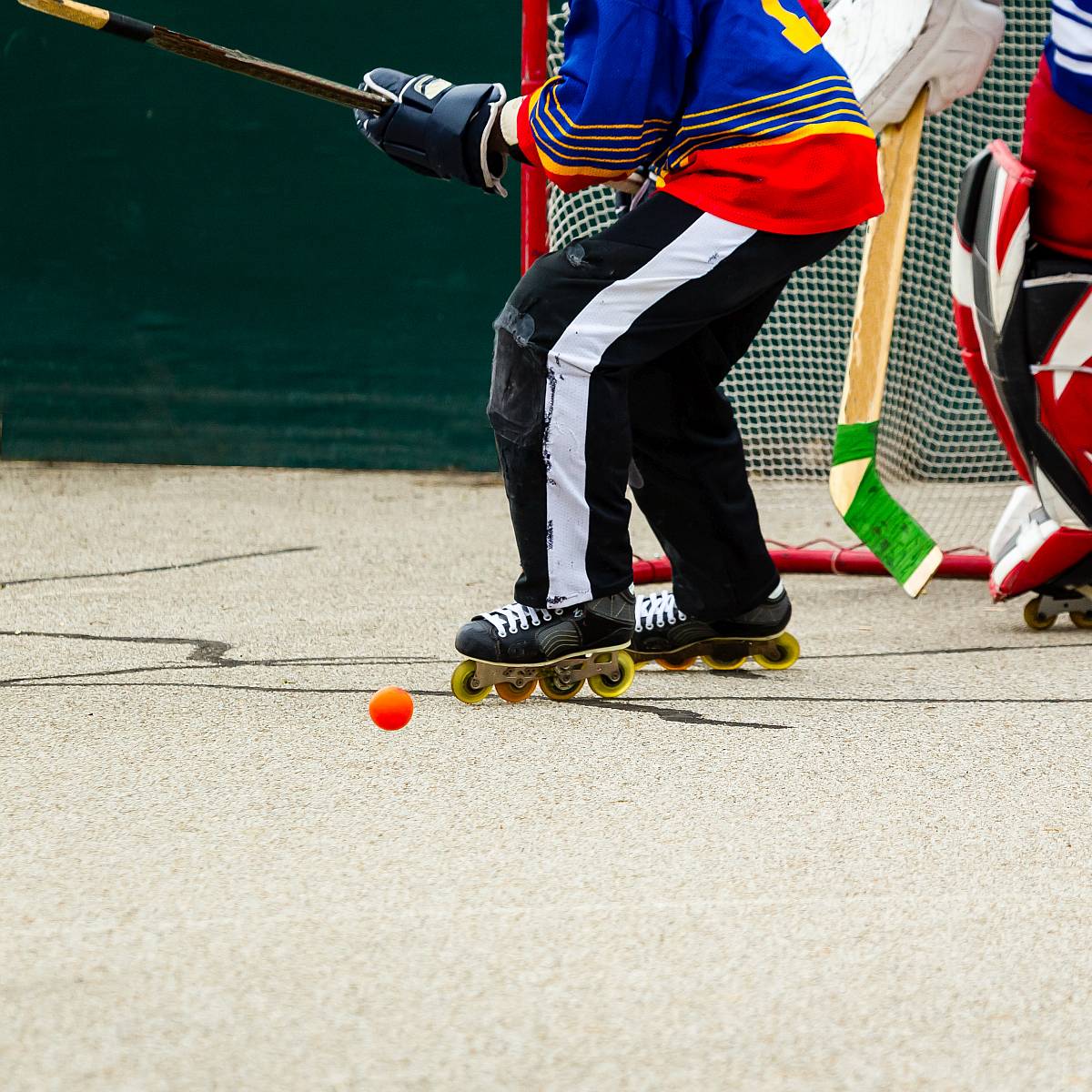 Zwei Personen spielen vor einem Tor Inline-Hockey in Schutzkleidung